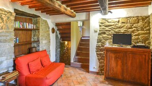 Um quarto acolhedor com um sofá vermelho, uma estante de madeira, uma parede de pedra, uma escada e uma TV sobre um armário de madeira.
