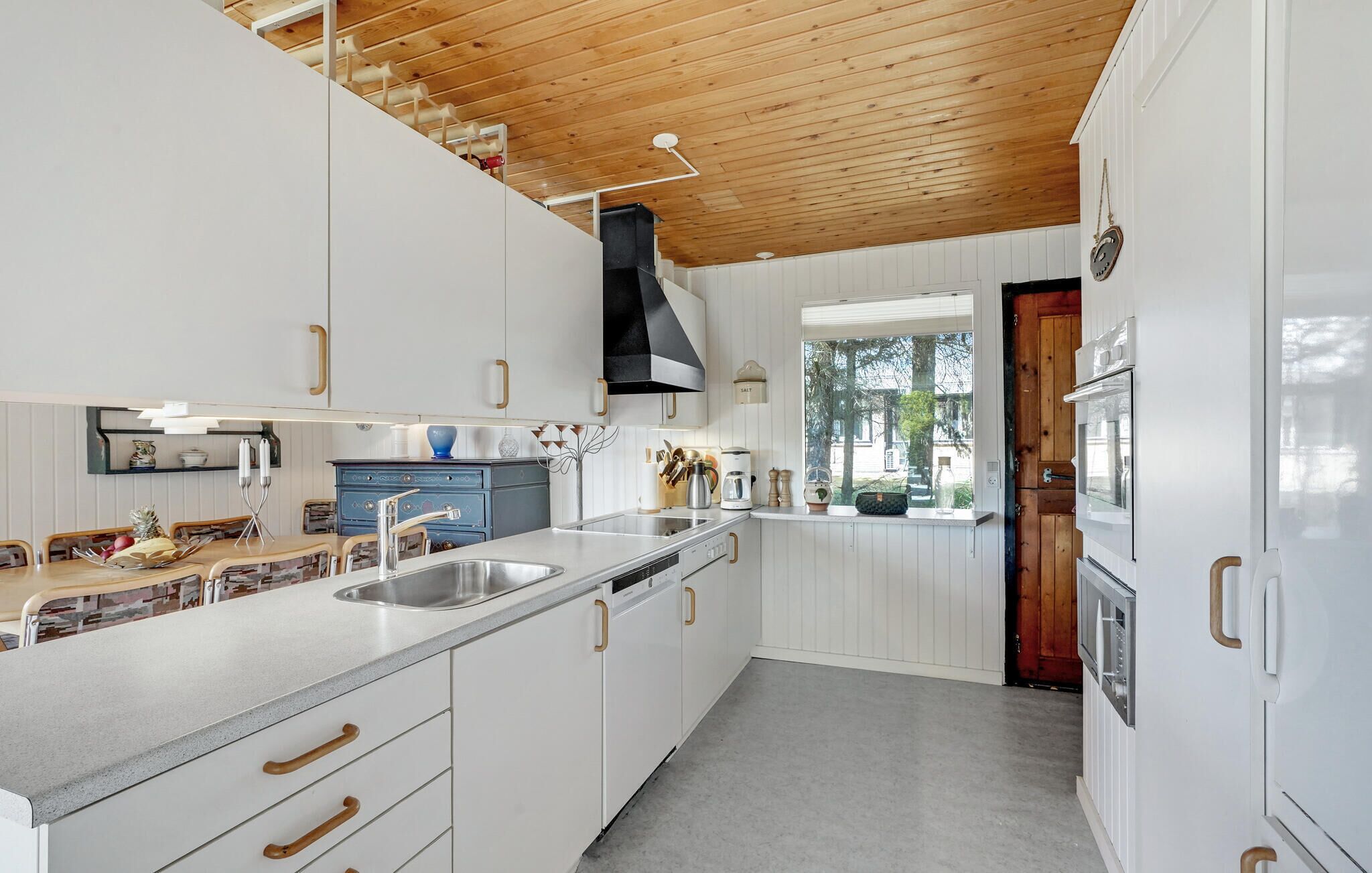 Une cuisine moderne avec des meubles blancs, un plafond en bois et une fenêtre donnant sur un espace verdoyant.
