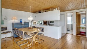 Ett modernt kök med vita skåp, ett träpanelat tak och en matplats med ett träbord och metallstolar.