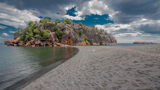 Una spiaggia con un'isola rocciosa e acqua cristallina.