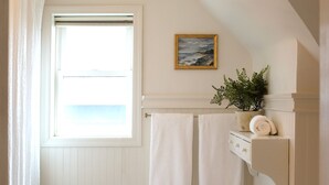 Un bagno con pavimento piastrellato in bianco, una finestra vista, un portasciuga, un piccolo sgabello e una pianta in vaso.