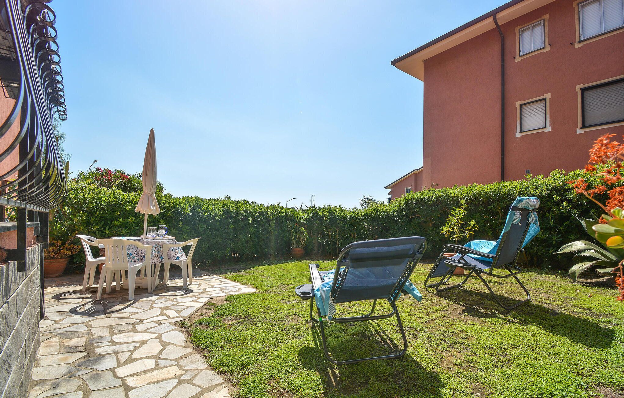 A patio with a stone pathway, a table with chairs, and a lounge chair.