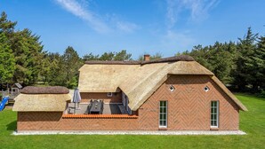 A thatched-roof house with a brick exterior, a patio with outdoor furniture, and a small play area with a slide. - Gorgeous home in Ulfborg with kitchen (Ulfborg)
