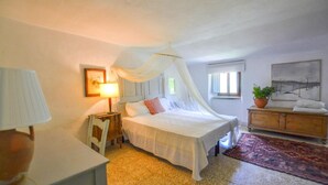 Una camera da letto con un letto a baldacchino, un comodino con una lampada, una cassettiera, un tappeto e un quadro appeso al muro.