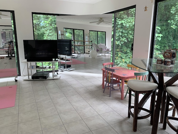 Un amplio salón con una gran televisión de pantalla plana, una mesa de vidrio y sillas.