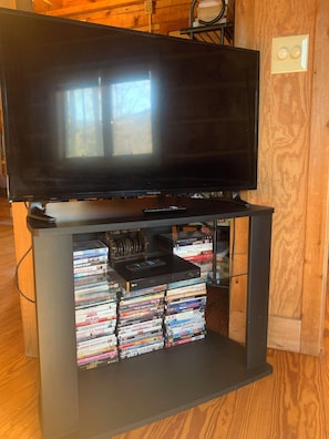 A television on a wooden stand with a shelf below holding a stack of DVDs.