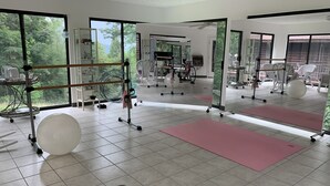 Een ruime fitnessruimte met trainingsapparatuur, grote ramen en een betegelde vloer.