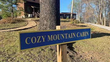 A sign for 'Cozy Mountain Cabin' in a wooded area with a cabin in the background.