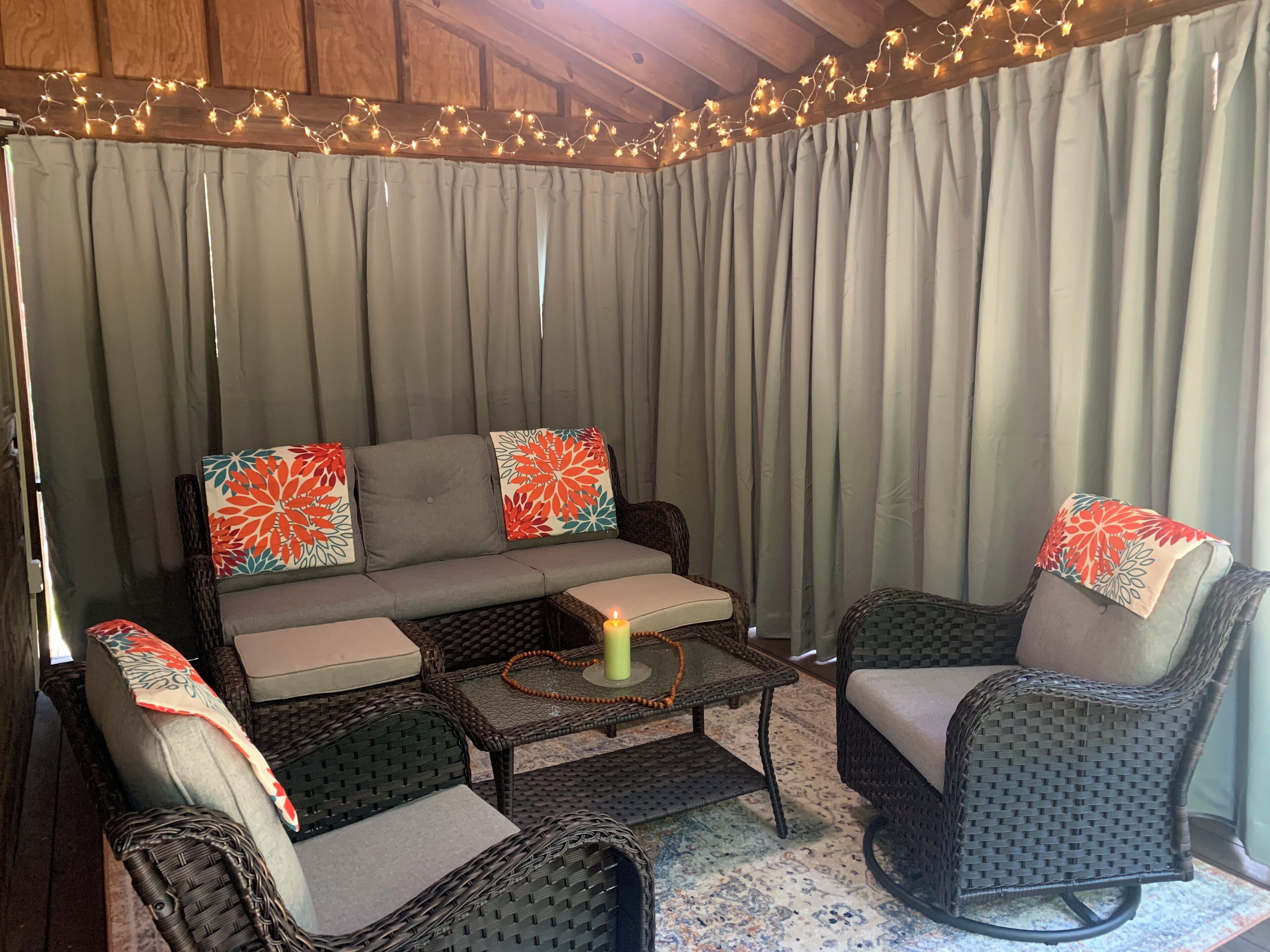 Un rincón acogedor con un sofá, dos sillones, una mesita con una vela y una guirnalda decorativa de luces.