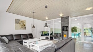 Una sala de estar moderna con un sofá modular, un televisor de pantalla plana, una chimenea y vistas a una piscina exterior.