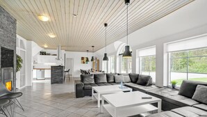 Una sala moderna con chimenea de piedra, un sofá grande y un comedor con cocina al fondo.