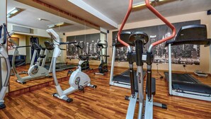 A gym with various exercise machines, wooden flooring, and cityscape murals on the walls.