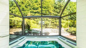 A hot tub with a glass enclosure, surrounded by a lush green landscape.