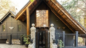 A rustic cabin with a steeply pitched roof, stone pillars, and a black front door.