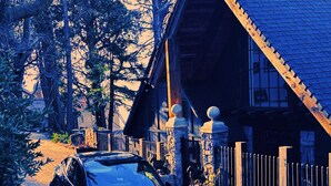 A car parked in front of a wooden cabin with a stone fence and a stone statue.