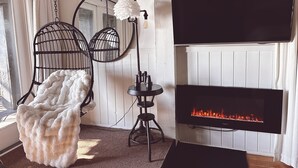 A cozy living room with a fireplace, two hanging chairs, a round mirror, and a flat-screen TV.