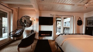 A bedroom with a large bed, a hanging chair, a fireplace, and a TV.