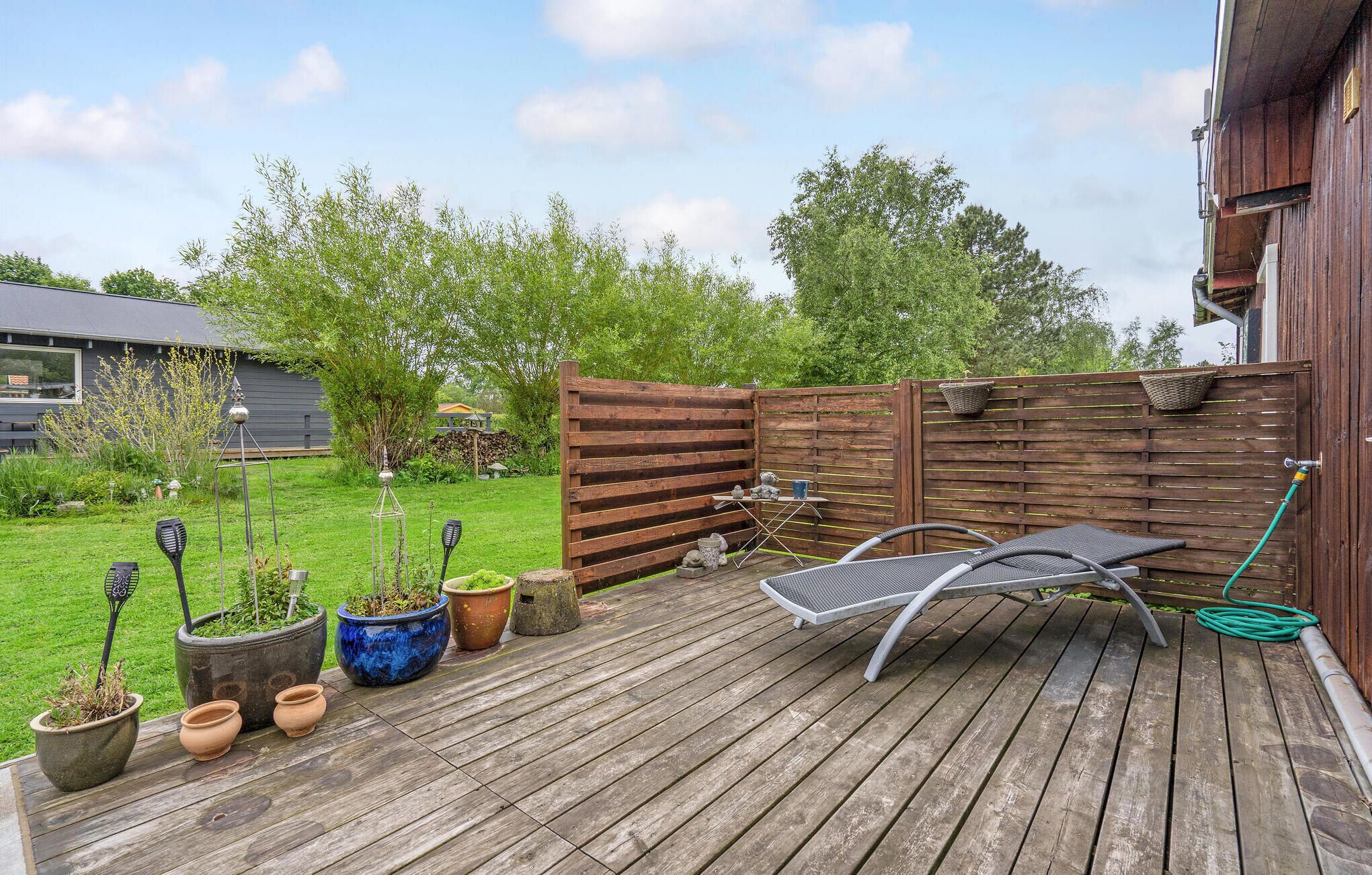 A wooden deck with outdoor furniture, potted plants, and a wooden fence.