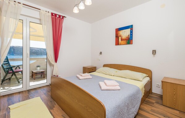 A bedroom with a wooden bed, a nightstand, a bedside table, a chair, and a view of the sea through a glass door.