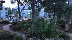 A residential area with a swimming pool, palm trees, and a multi-story building with balconies. - Myrtle Beach Resort Unit 6201 - Ocean Getaway (Myrtle Beach)