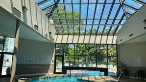 An indoor swimming pool with a glass ceiling, safety signs, and a view of the outdoors. - Myrtle Beach Resort Unit 6201 - Ocean Getaway (Myrtle Beach)