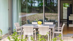 A modern outdoor dining area with wicker chairs and a table, overlooking a beach and forest. - 2 bedroom amazing apartment in Binz OT Prora (Binz OT Prora)
