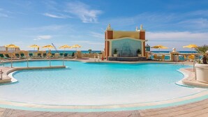 Ein großer Pool im Freien mit einer zentralen Fontäne, umgeben von Liegestühlen und Sonnenschirmen.