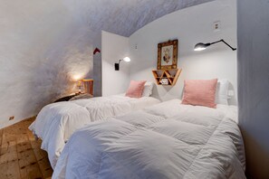 Un dormitorio con dos camas, ropa de cama blanca, suelo de madera, una lámpara de pared y un cuadro enmarcado.