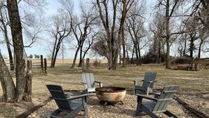 Et udendørs opholdsområde med Adirondack-stole og et bålsted.