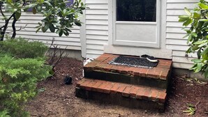 Une maison avec un porche à l’avant, une fenêtre avec des volets violets et des jardinières suspendues.