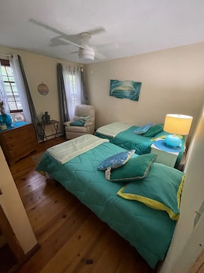 Ein Schlafzimmer mit zwei Betten, einem Deckenventilator, einem Stuhl, einem kleinen Tisch und einer Lampe.