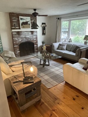 Ein gemütliches Wohnzimmer mit Kamin, einer Couch, einem Couchtisch und einem Holznachttisch.