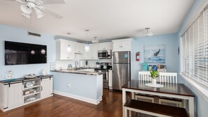 A modern kitchen with white cabinetry, a stainless steel refrigerator, and a dining area with a wooden table and bench. - 300ft to the Beach • Central A/C, Linens & Towels, Beach Badges & Gear Included (Seaside Heights)