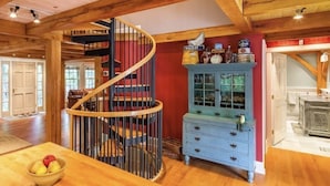 Un intérieur en bois avec un escalier en colimaçon, un buffet bleu aux portes vitrées et une table en bois sur laquelle se trouve un saladier rempli de fruits.