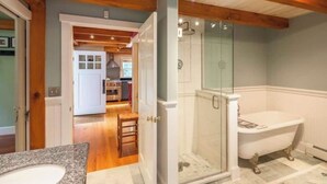 Une salle de bain avec une douche à parois de verre, une baignoire blanche et un banc en bois.