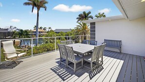 Una terraza con mesa y sillas, con vista a un cuerpo de agua y palmeras.
