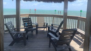 A wooden deck with four chairs and a table, overlooking a beach with a thatched roof pavilion. - 🏝️OCEANFRONT PARADISE AWAITS YOU🏖️ (Tavernier)