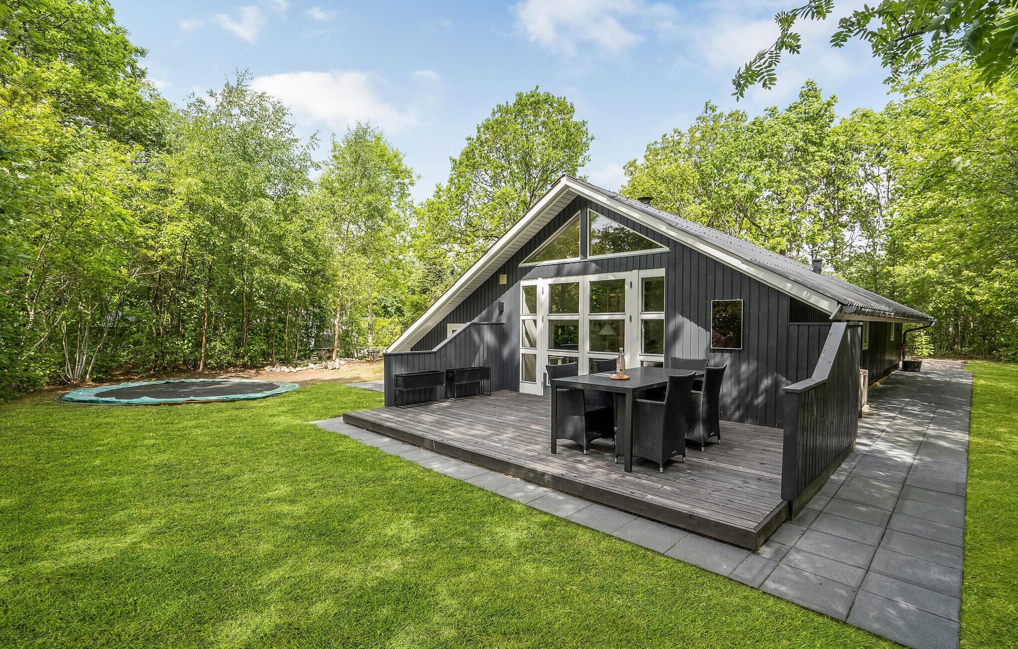 Een moderne, donkere cabin met een grote schuifdeur, een terras en een trampoline in de achtertuin.
