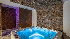 Une salle de spa moderne avec un mur en pierre, un jacuzzi et un plafond avec des poutres apparentes.