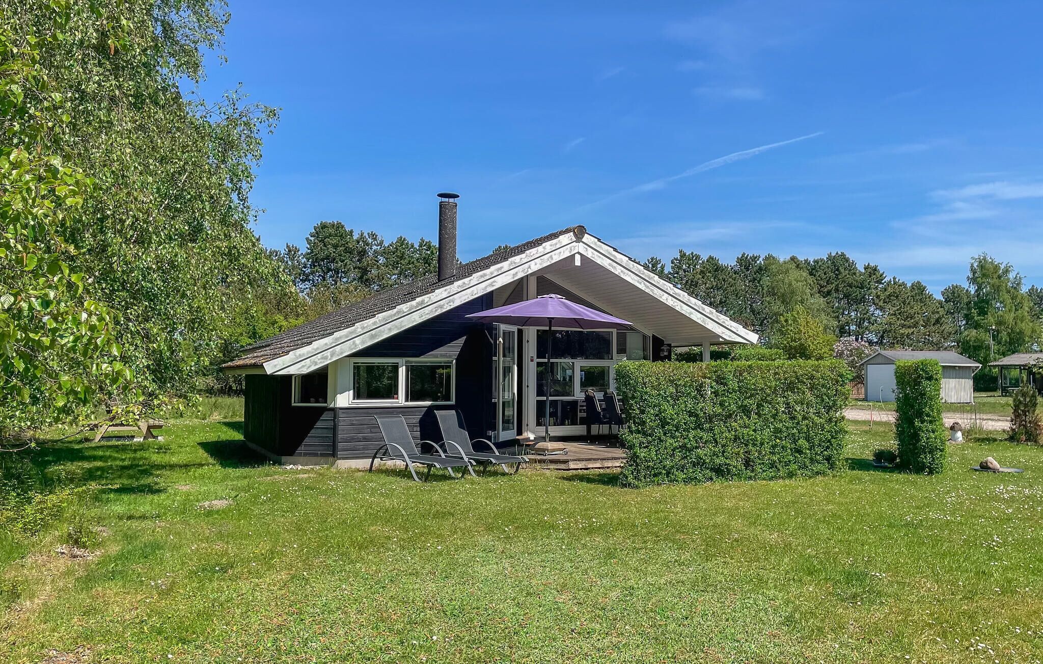 A house with a sloped roof, a covered porch with a purple umbrella, and a lawn.