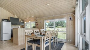 A wooden interior with a dining table, chairs, a kitchen area, and large windows. - Amazing home in Rødby with sauna (Rødby)