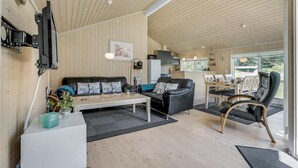 A modern living room with a wooden ceiling, a black leather sofa, a white coffee table, and a dining area with a white table and chairs. - Amazing home in Rødby with sauna (Rødby)