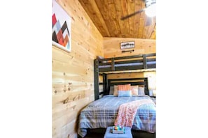Quarto estilo cabana de madeira, com cama, uma mesinha e um ventilador de teto.
