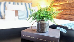 Ein rustikales Holzinterieur mit einem Bett, das mit gestreifter Bettwäsche bezogen ist, einer kleinen Topfpflanze auf einem Buch und einer Holzwand.