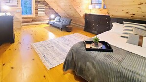 A cozy attic bedroom with wooden beams, a bed, a sofa, and a small table with a plant. - Three Bears Cabin - Unique Four Bedroom Luxury Cabin with Hot Tub! (Pickens)