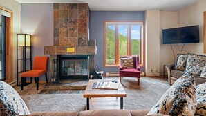 Un salón con chimenea, televisor y una ventana grande con vista a árboles.