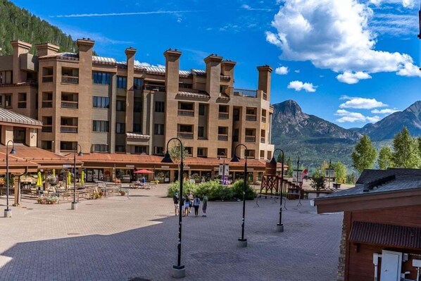 Un hotel de varios pisos con un patio central, mobiliario exterior y vistas a la montaña.