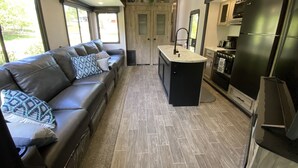 A compact kitchen with a central island, a built-in oven, and a refrigerator. - 2022 5th Wheel RV, 2BD, Sleeps 6, Kootenai River Views/Access, Picnic Table (Bonners Ferry)