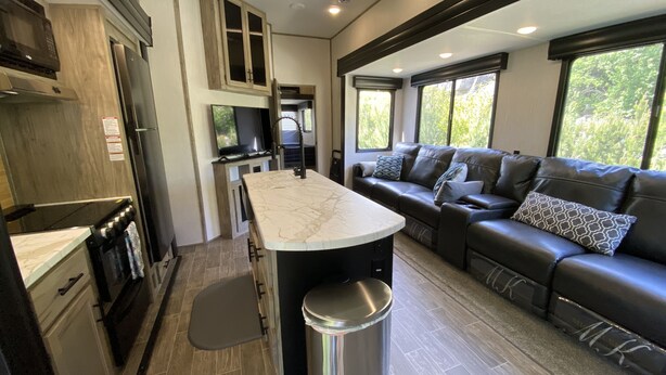 A modern kitchen with a marble countertop, stainless steel appliances, and a built-in seating area with a leather couch and patterned pillows. - 2022 5th Wheel RV, 2BD, Sleeps 6, Kootenai River Views/Access, Picnic Table (Bonners Ferry)