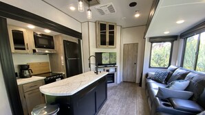 A compact kitchen with a central island, built-in appliances, and a seating area with a view. - 2022 5th Wheel RV, 2BD, Sleeps 6, Kootenai River Views/Access, Picnic Table (Bonners Ferry)